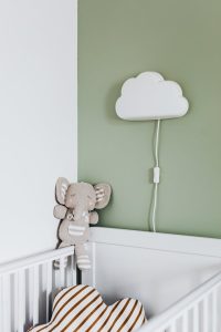 Tranquil nursery corner featuring an elephant plush toy and cloud-shaped wall light above a crib.