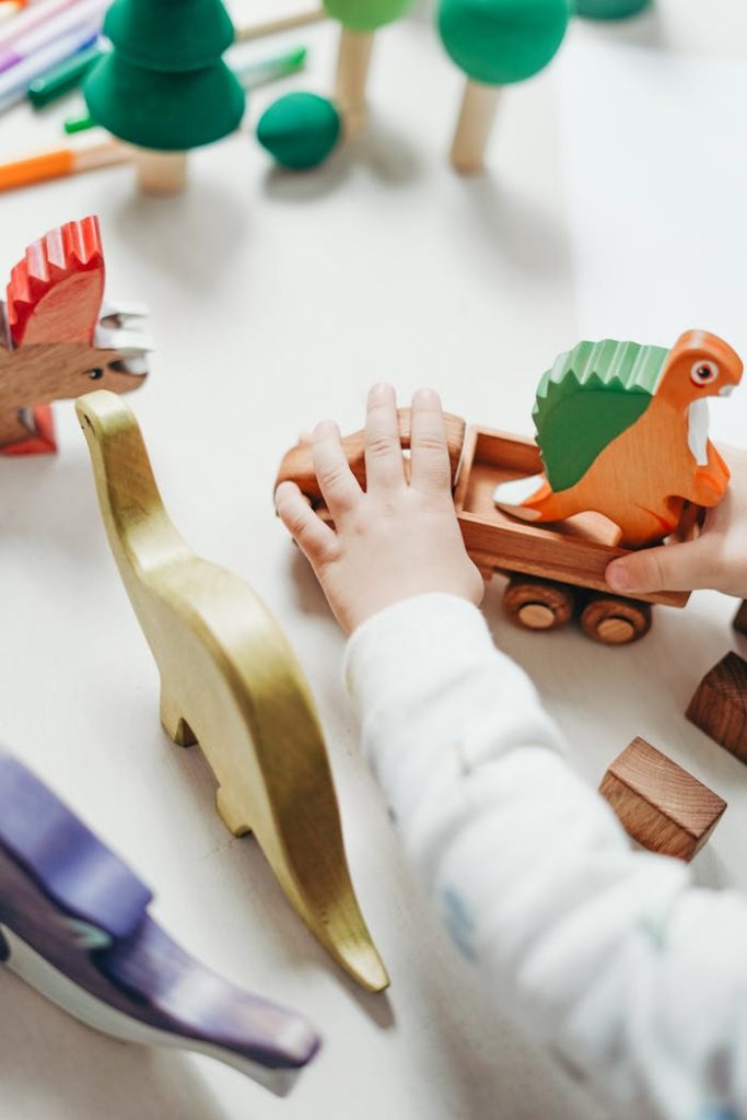 Childs hands interact with vibrant wooden toy dinosaur set, creating playful scene on tabletop.